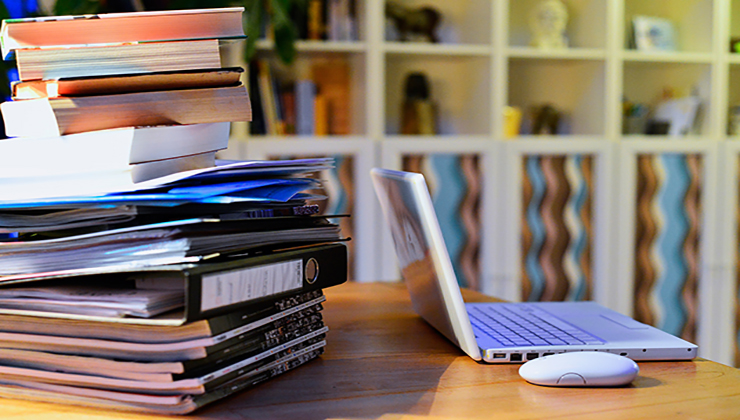 Een bureau met een stapel publicaties en een laptop